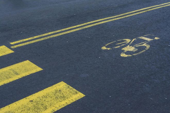 Bike lane with yellow markings on an empty asphalt road, showing bicycle symbol and zebra crossing.