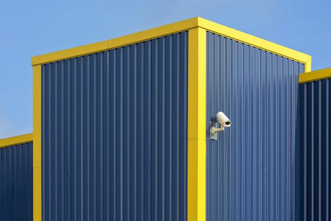 Close-up of a modern blue and yellow building facade with a mounted security camera.